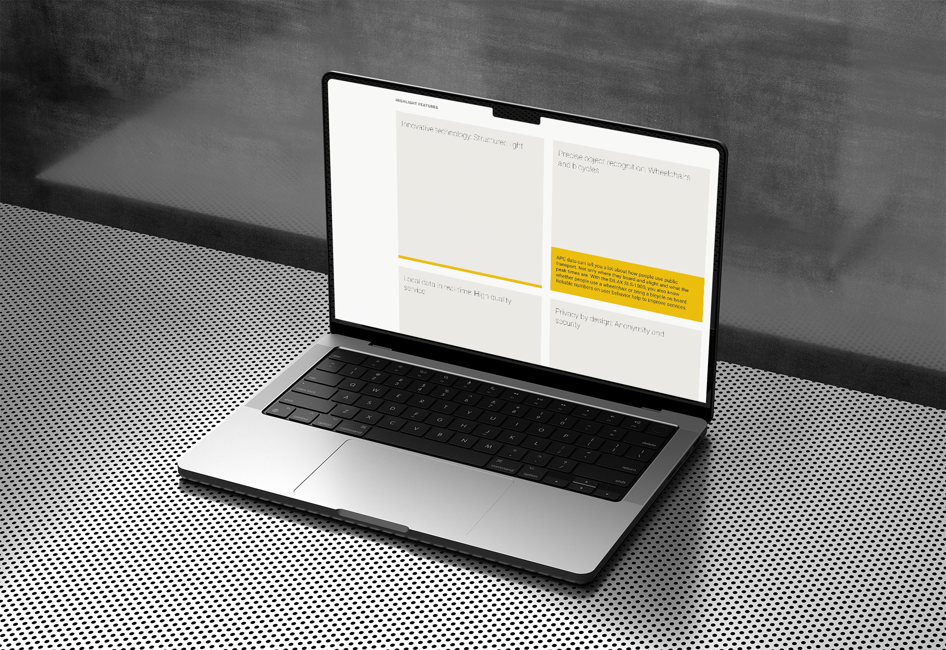 A mockup of a laptop in a cool metallic environment. The screen shows a very clean website consisting of four grey square navigaiton tiles on the right with some text in a smaller yellow section.