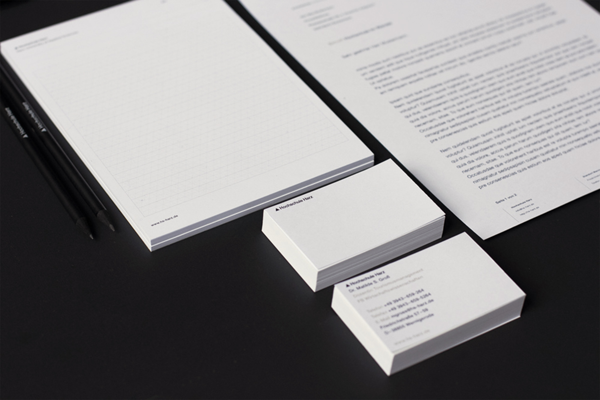 A business letter, business cards, a branded notepad and branded pencils on a black background.
