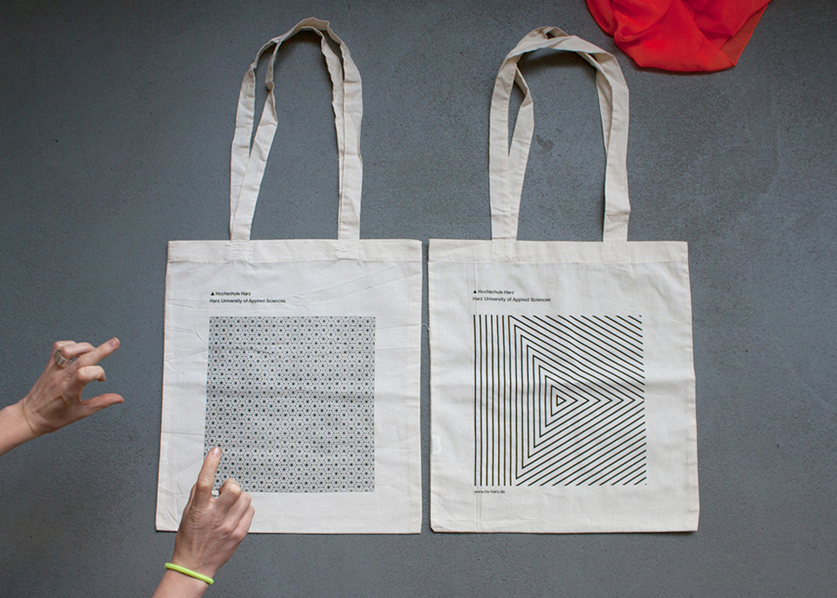 Two totebags with a branded print from Hochschule Harz lay on a table. The designs are geometrical and monochrome.
