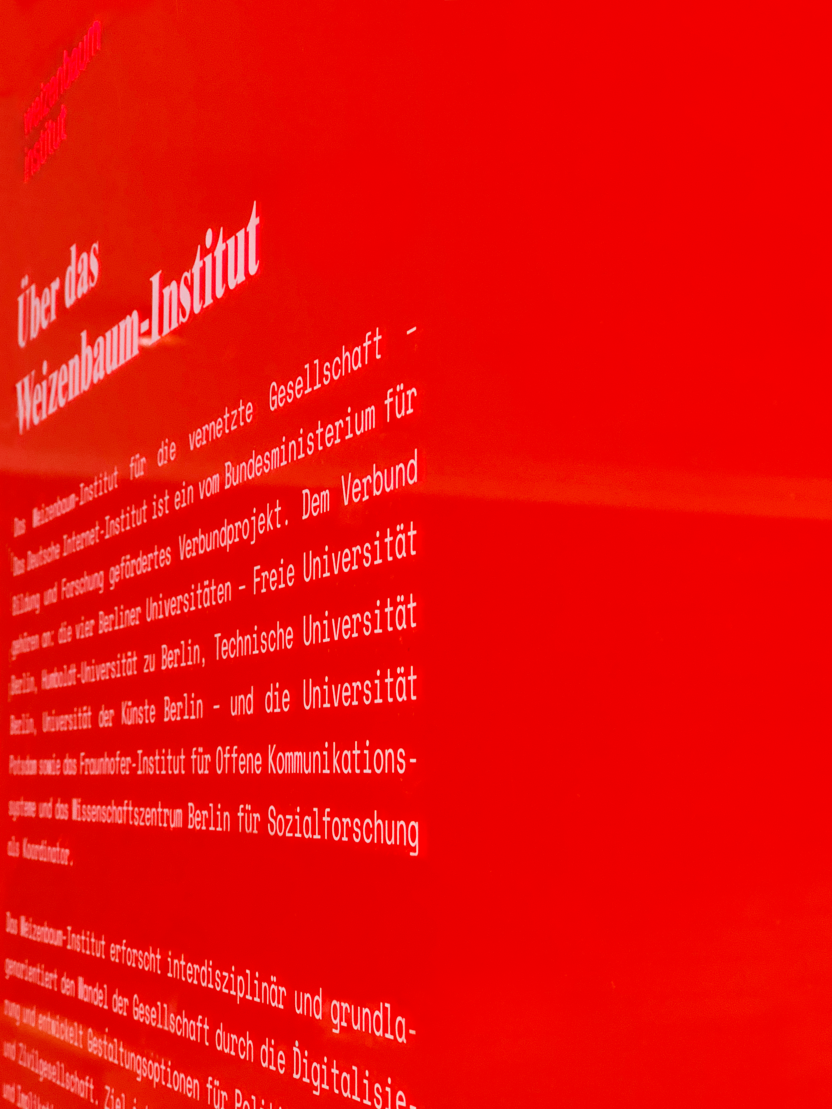 A photo taken from the side showcasing a semi-transparent red acrylic poster that features a title and 2 text paragraphs.